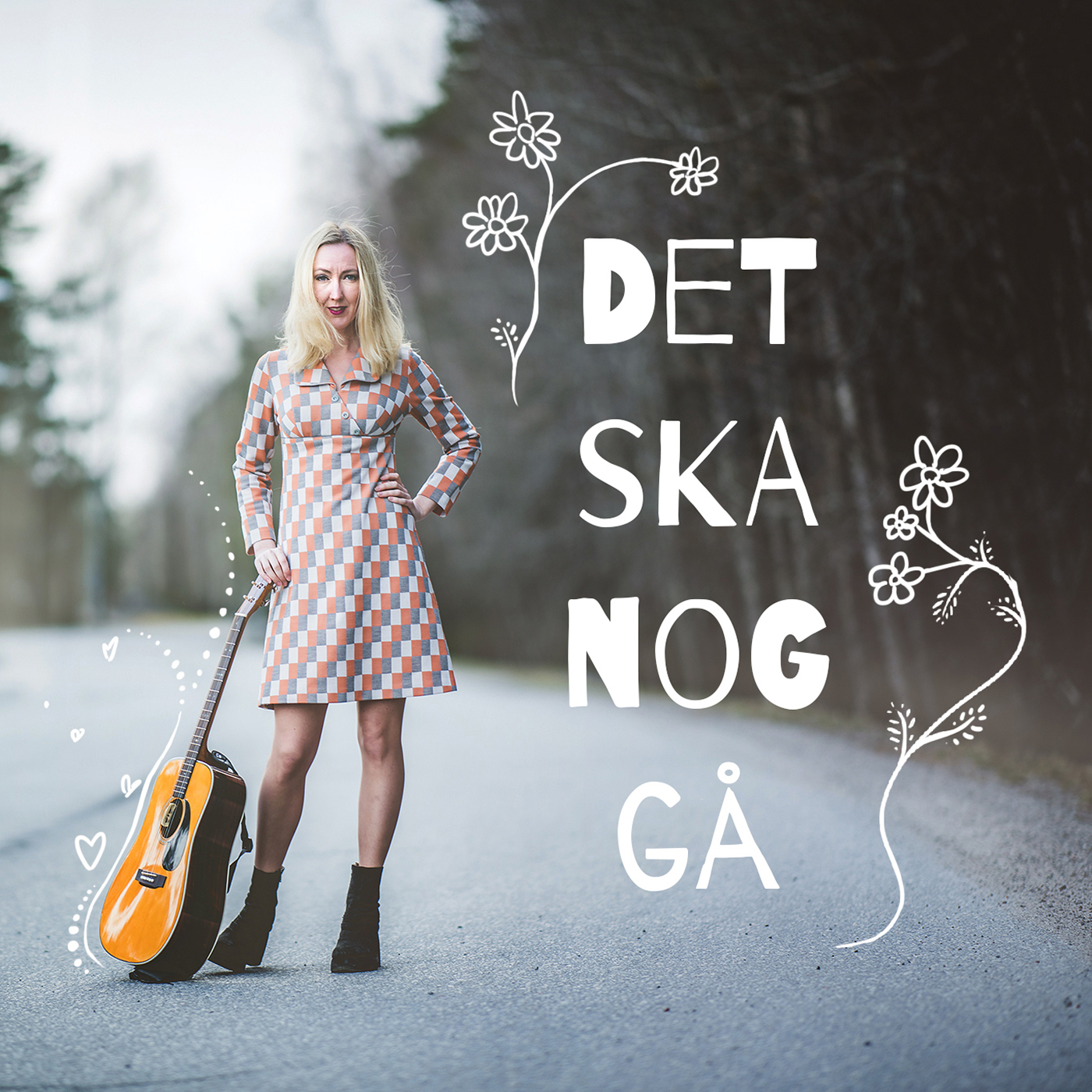 Det ska nog gå Kajsa Larsson. Kajsa står mitt på en gata och håller en gitarr som står på marken. Texten Det ska nog gå, står skriven på bilden och har ritade blommor runtomkring.